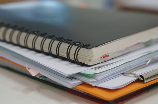 Stack of paperwork and notebook placed on white desk at office.