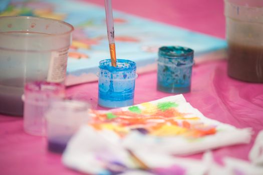 Watercolor paint in plastic cans on the pink table. 