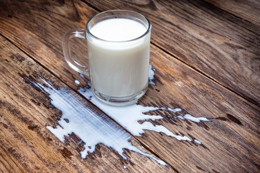 glass of milk has spilled a wooden surface.