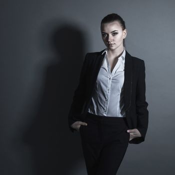 Portrait of young businesswoman in black suit on dark background