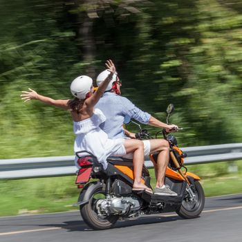 Cheerful couple riding scooter at countryside road, vacation concept