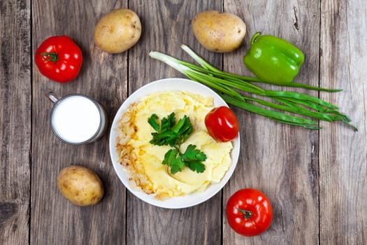 mashed boiled potato with herbs. milk and vegetables on a wooden background