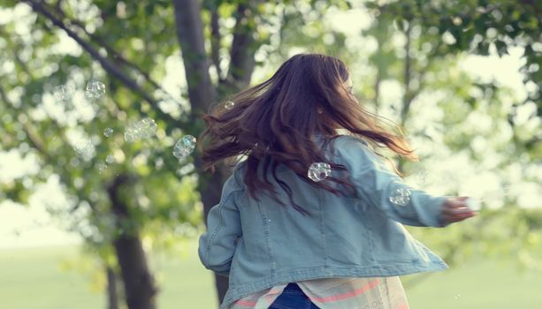 Young girl play with soap-bubbles in forest