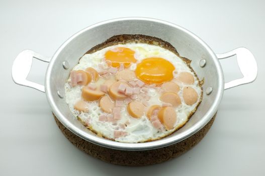 Fried egg with ham and sausage in a pan