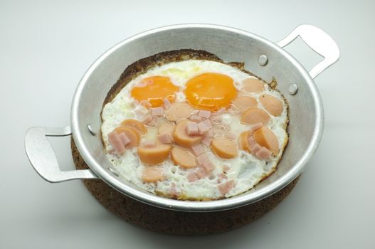 Fried egg with ham and sausage in a pan