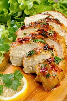 Slices of roasted chicken breast on a wooden board with fresh herbs