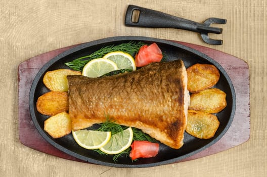 Fried fish with fries,lemon, dill and ginger in a pan lies on the blackboard and wooden background.