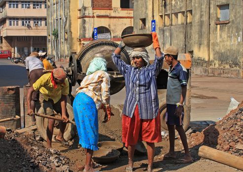 Indian woman labourer carrying metal bowl on head. Bowl is  filled with cement. Vasco da Gama, Goa, India.