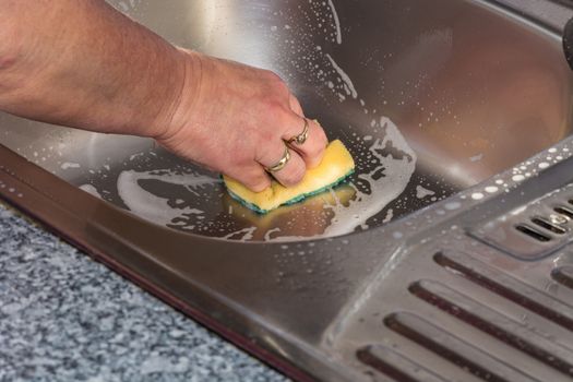 Cleaning a kitchen sink with yellow sponge