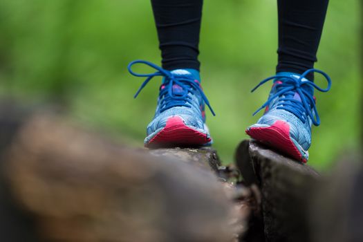 Adventure, sport and exercise. Detail of female legs wearing sport shoes standing on tree trunk in forest.