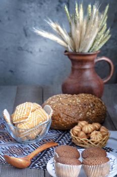Different cookies and bread, on old boards and towel, rustic style, bokeh. Jug and cereal ears.