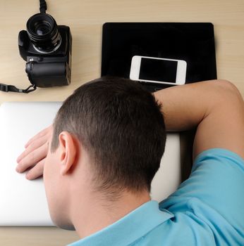 Person sleep on laptop next to camera and tablet on wood table