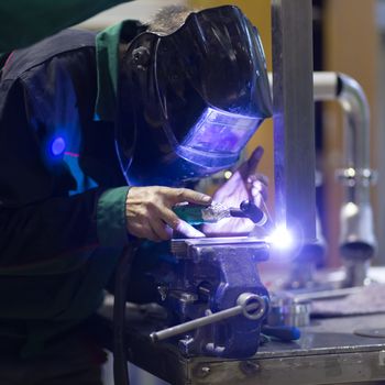 Industrial worker with protective mask welding inox elements in steel structures manufacture workshop.