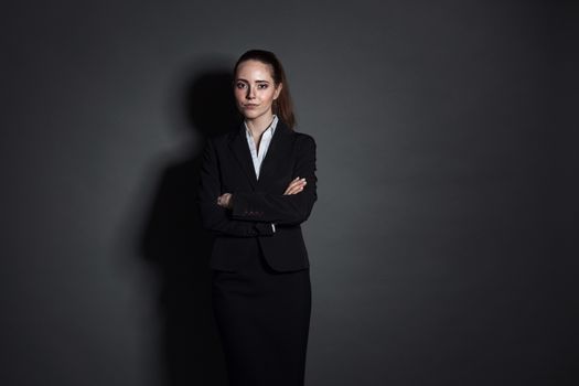 Portrait of young businesswoman in black suit on dark background