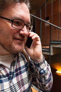 A young man with glasses searching around and laughing and talking by phone