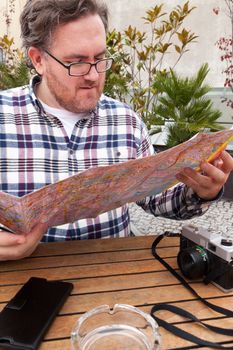 Young traveller man with glasses and a hat  looking for a place in a map looking up