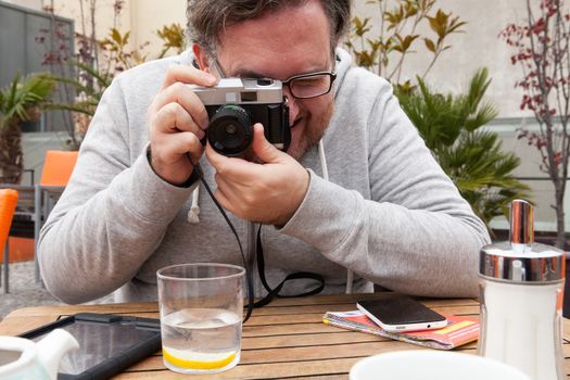 Young traveller man with glasses looking and laughing is having fun with a vintage camera