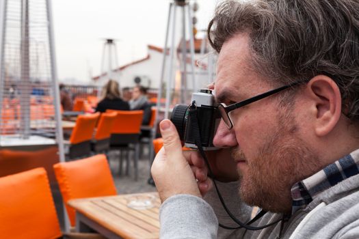 Young traveller man with glasses looking and laughing is having fun with a vintage camera