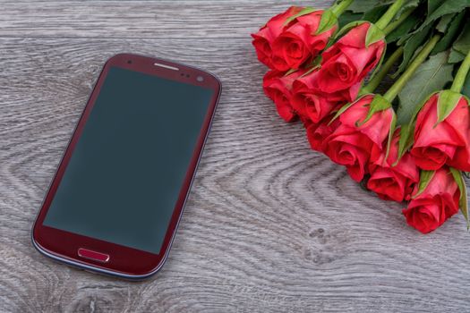 Red mobile phone and roses on a grey wooden background