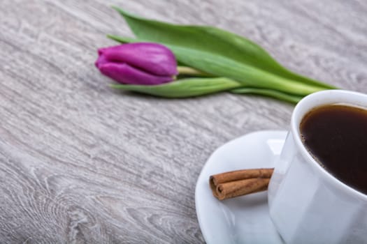 A cup of coffee with cinnamon and purple tulips on a wooden background