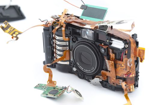 Compact point and shoot camera with disassembled parts on pulled out circuit board and buttons over white background