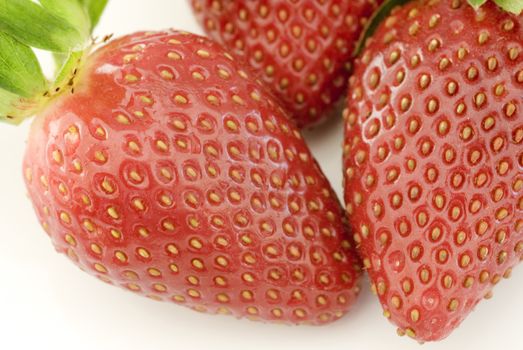 Extreme close up on glossy skin and seeds on three fresh strawberries over white background