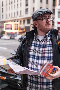 Young traveller man with glasses and a hat  looking for a place in a map looking up