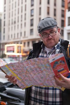 Young traveller man with glasses and a hat  looking for a place in a map looking up