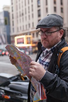 Young traveller man with glasses and a hat  looking for a place in a map looking up