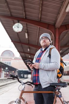 A young man with glasses and a hat is coming into a wagon-train with his bike in a urban scene