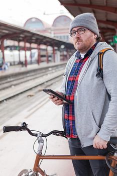 A young man with glasses and a hat is coming into a wagon-train with his bike in a urban scene