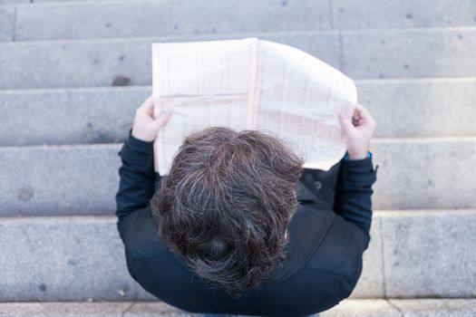 A young businessman with glasses reading a newspaper is thinking and talking by smartphone  in urban scene