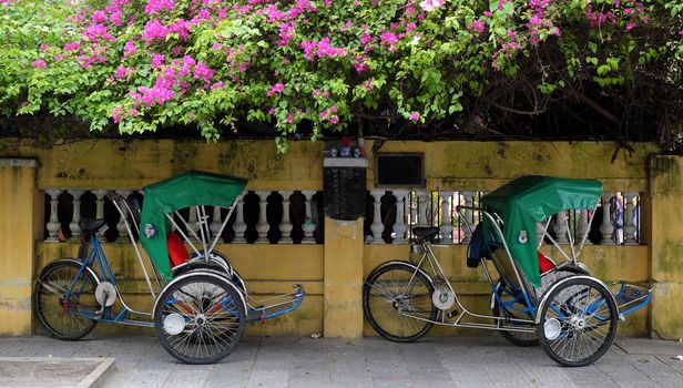 Nice scene at Hoi An old town, a famous place for Vietnam travel, pedicab park on pavement under flower trellis, pedicab is eco transport vehicle that friendly with environment