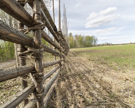 Swedish Farm Fence by Field with trees and a cloudy sky.