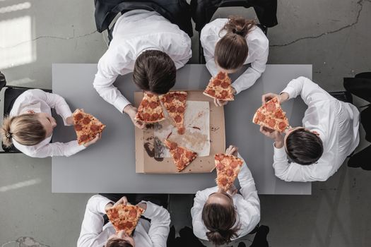 Business team eating pizza in office sitting around the table