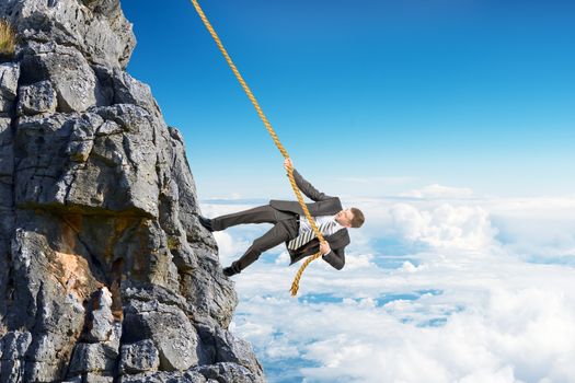 Businessman in suit climbing on mountain with rope 