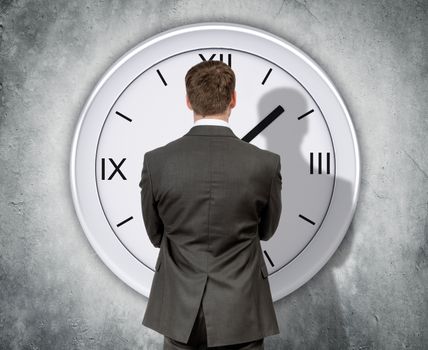 Businessman looking at clock on grey wall