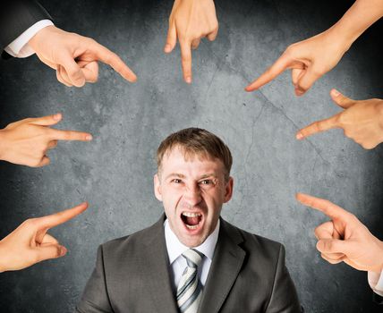 Many fingers pointing at screaming stressed businessman on grey background