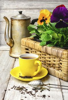 Yellow porcelain cup with tea and basket of decorative Pansy