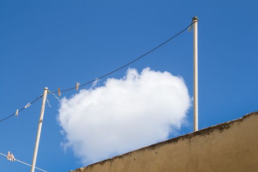 White cloud on a bright blue sky, seems like hanging and getting dry on a  clotheshorse at a roof of a house.