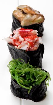 Various Japanese Sushi Gunkan Rolled Up in Nigiri with Seaweed, Shrimps and Mussels in Sauce closeup on Plank White background. Focus on Foreground