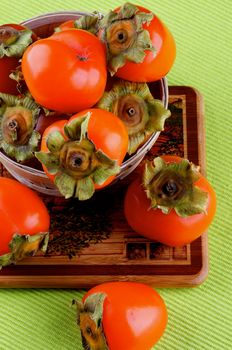 Delicious Raw Persimmon in Wooden Bowl closeup on Wooden Board and Green Textile Napkin background. Top View