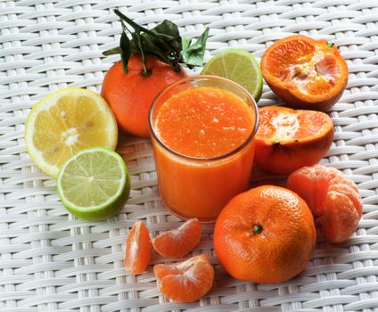 Glass of Freshly Squeezed Mixed Citrus Juice with Tangerines, Limes, Oranges and Lemons closeup on Wicker background