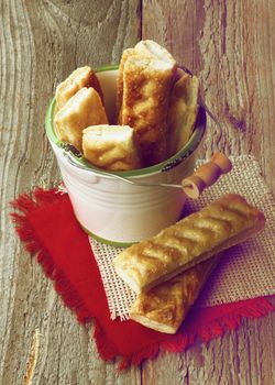 Puff Pastry Sticks Sprinkled with Sugar Crystals in White Bucket on Napkins closeup on Wooden background. Retro Styled