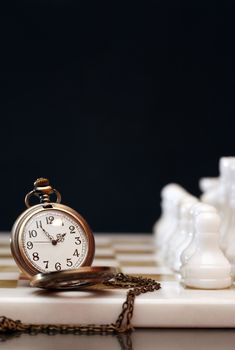 Vintage pocket watch on chessboard against dark background