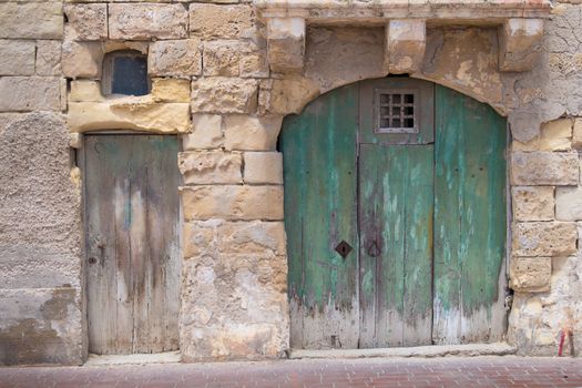 Street of an old fisher village at the island Malta, Marsaxlokk. Old green big gate with an arch and small traditional. Building made of stones.