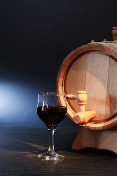 Nice oak barrel near wineglass with red wine on dark background