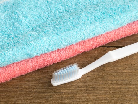 The blue and pink towel with white toothbrush on wooden plank background.