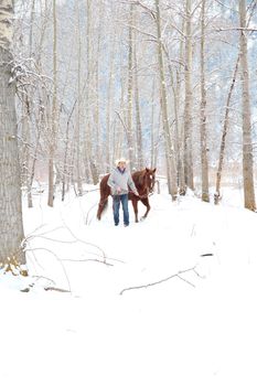 Young cowboy with his horse in a snow forest