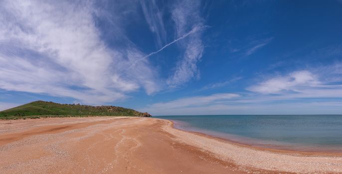 beach against a backdrop of mountains and blue sky with clouds